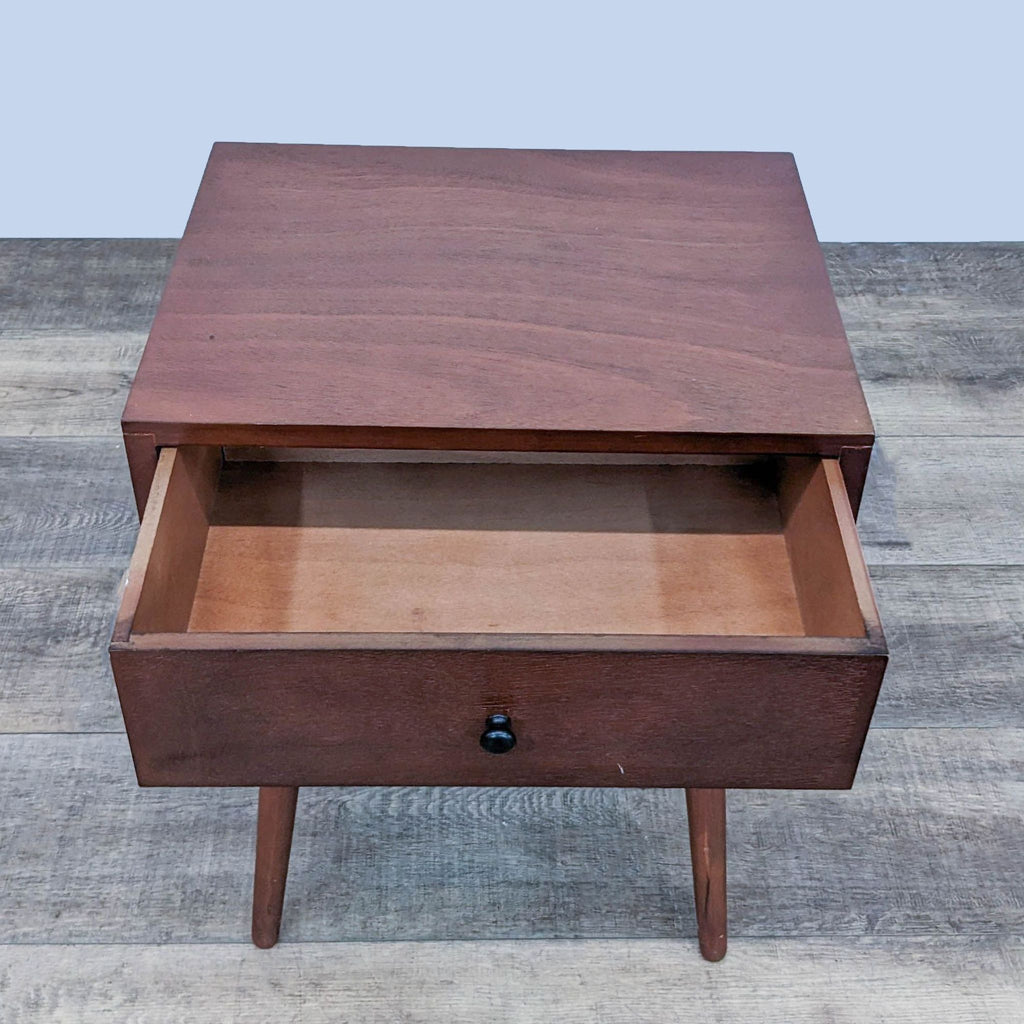a small, dark cherry wood bedside table with a drawer.