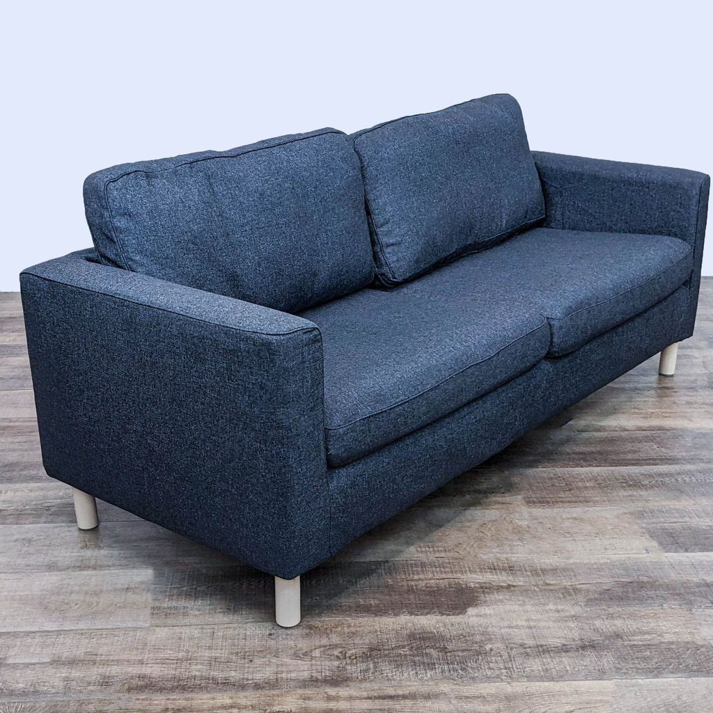 Angled view of dark gray sofa featuring removable cover and light finish legs.