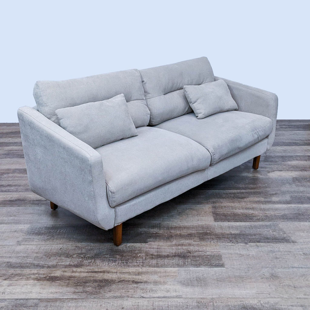 Low-profile beige fabric sofa, wood finish legs, narrow arms, and two pillows.