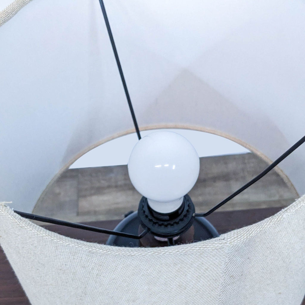 Top view of beige lampshade with visible light bulb and black supports.