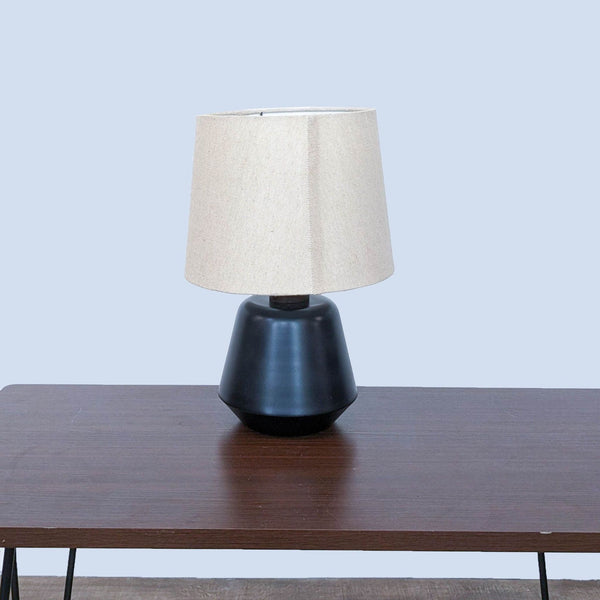 Reperch lamp with black base and beige shade on wooden table.