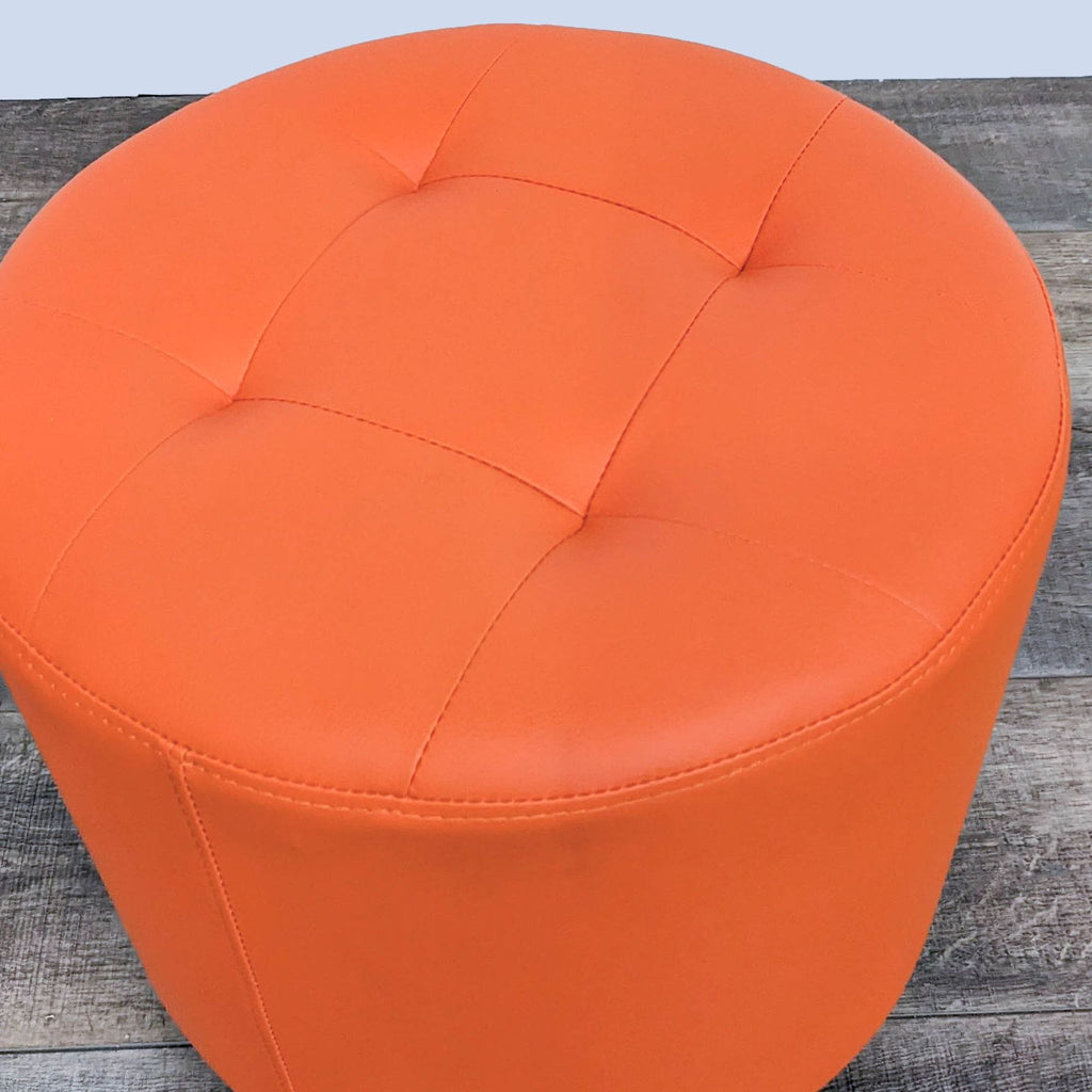 Close-up of the round, tufted top of an orange ottoman by Sunpan.