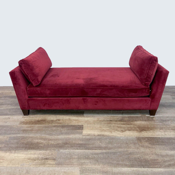 Red fabric daybed with bolster pillows and dark feet on a wooden floor.
