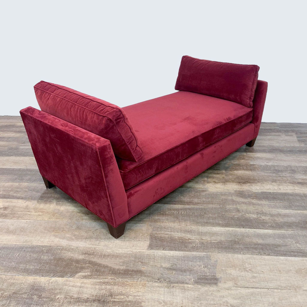Side view of red upholstered daybed featuring dark wooden legs.