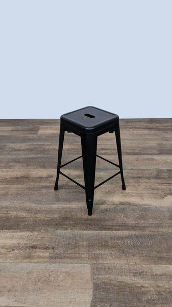 Black metal industrial-style stool with square seat on wooden floor.