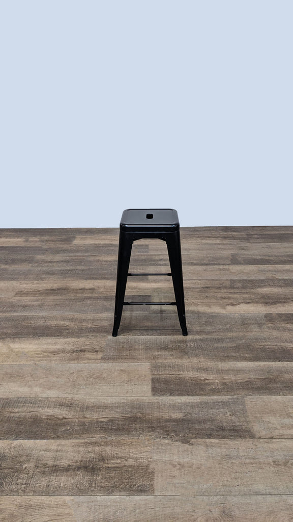 Side view of black metal stool on wooden floor, simple industrial style.