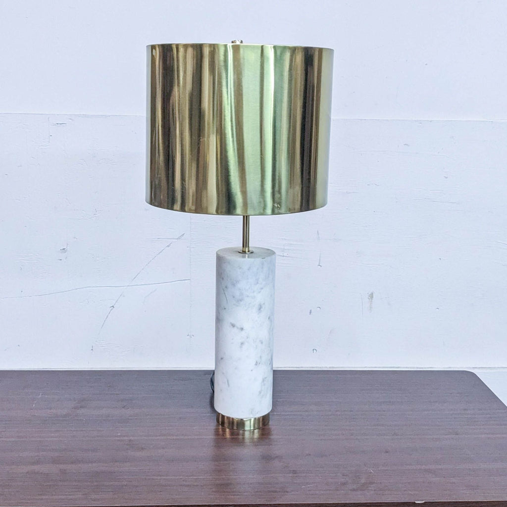 Reperch table lamp with a gold cylindrical shade and marble base on a wooden surface.