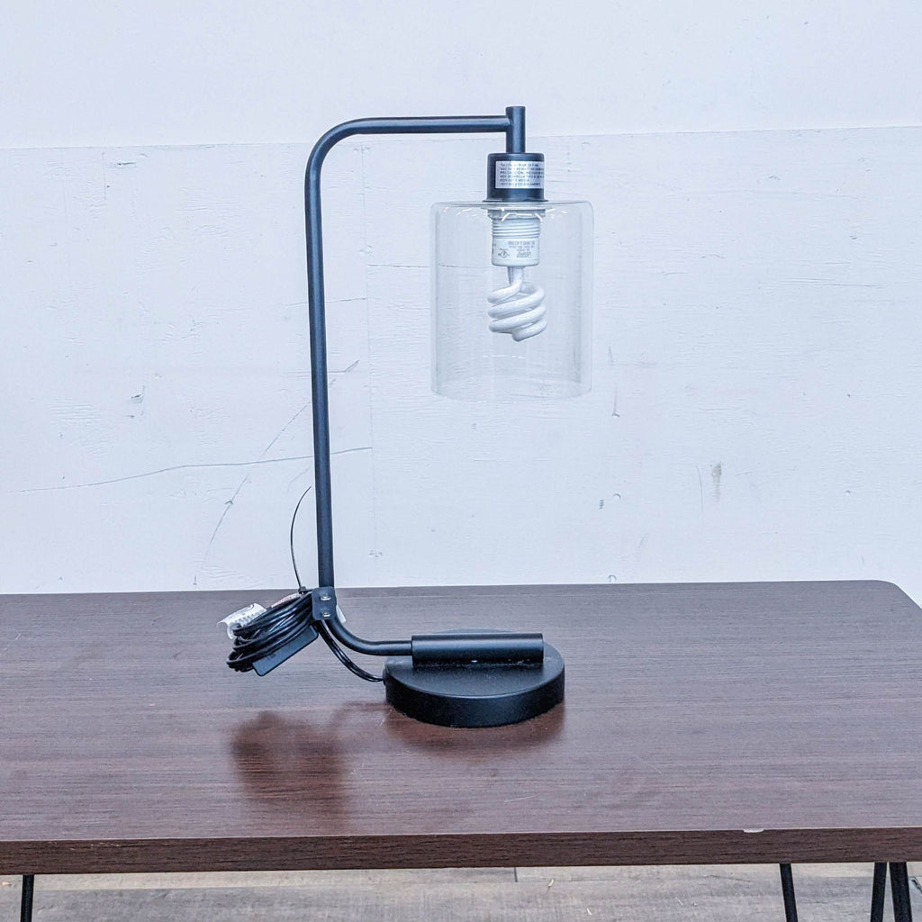 A Reperch lamp with a spiral bulb and clear glass shade on a wooden table.