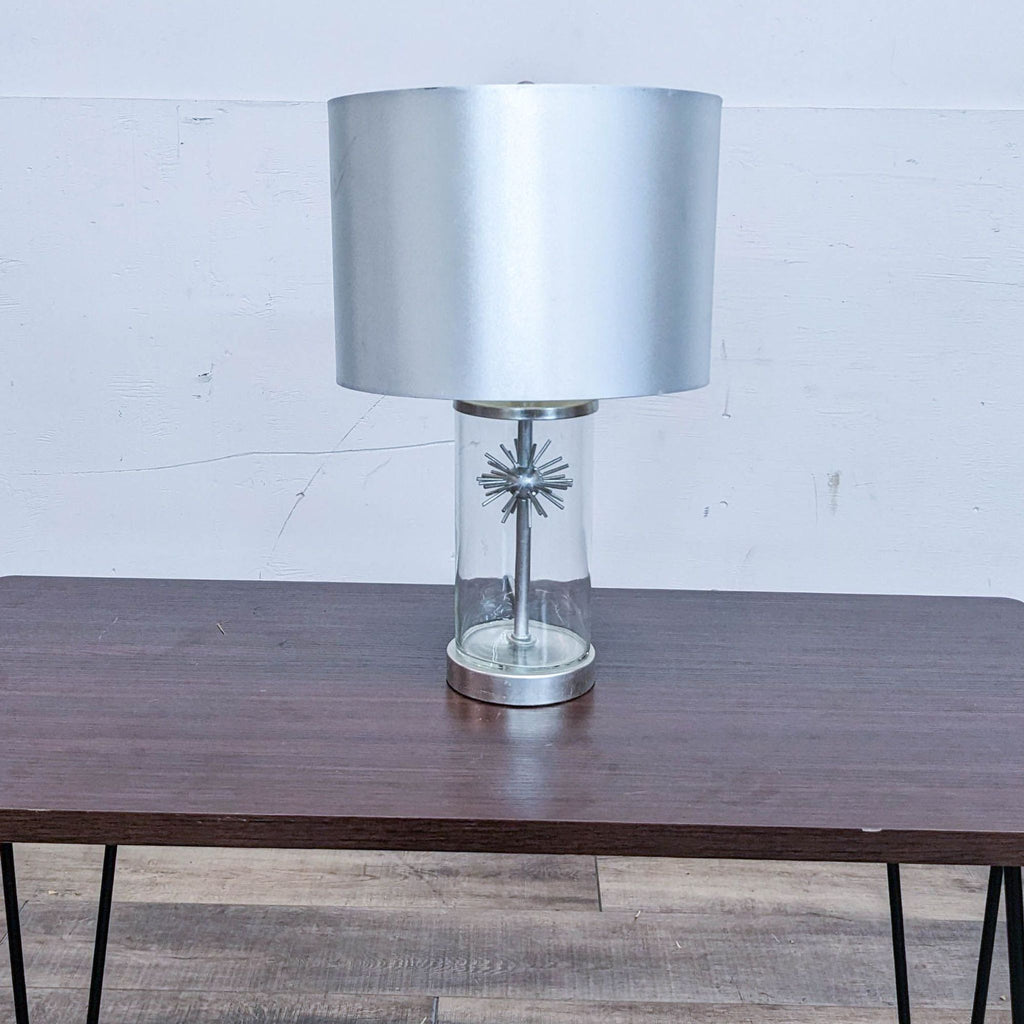 Reperch lamp with glass base and silver shade on a wooden table.