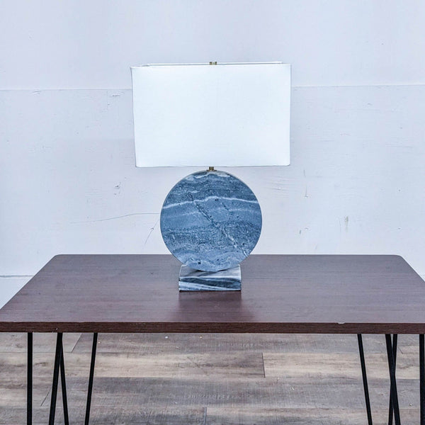 Reperch table lamp on wooden surface with blue stone base and white shade.