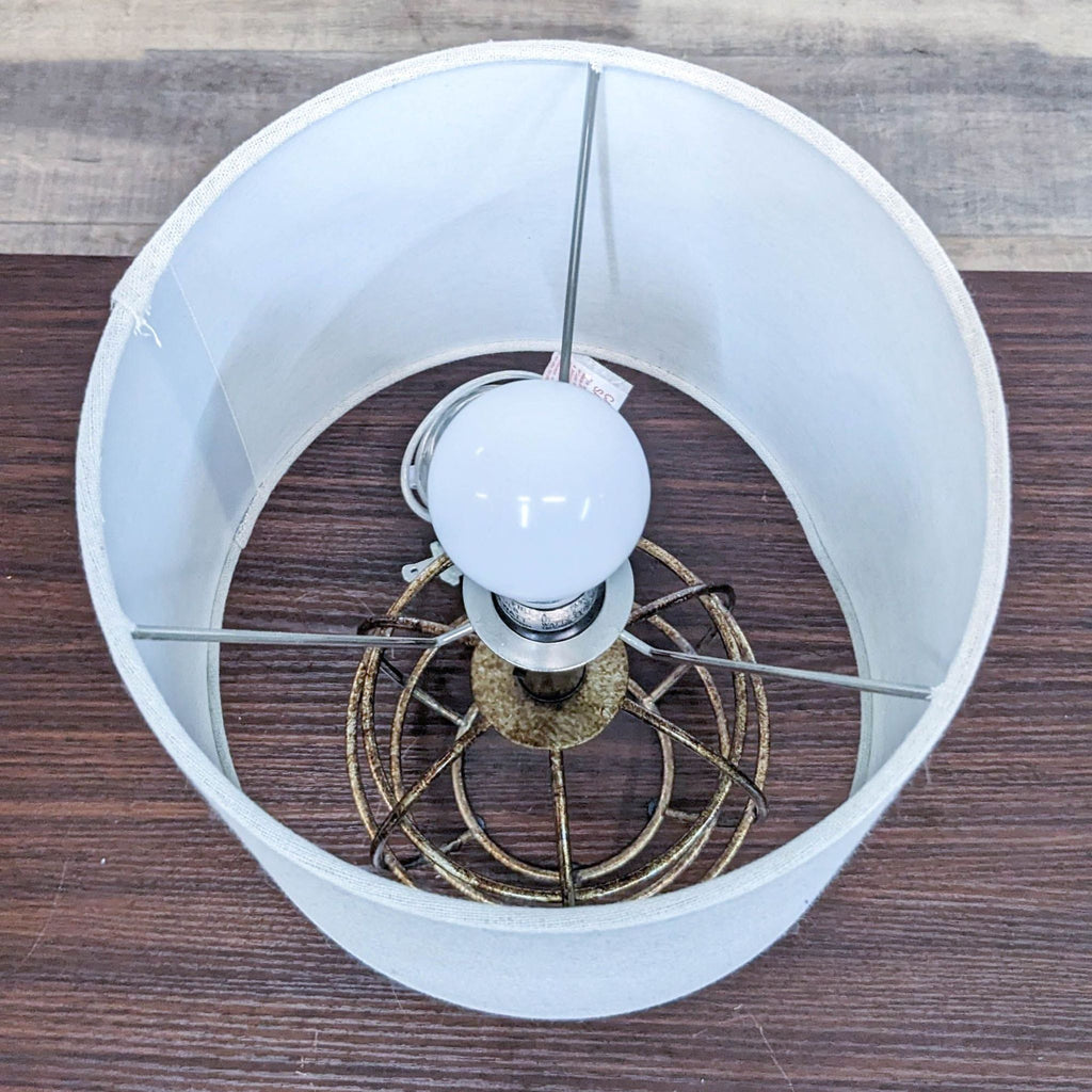 Top view of a lit bulb inside a Reperch lamp with a metal wire cage and white shade.