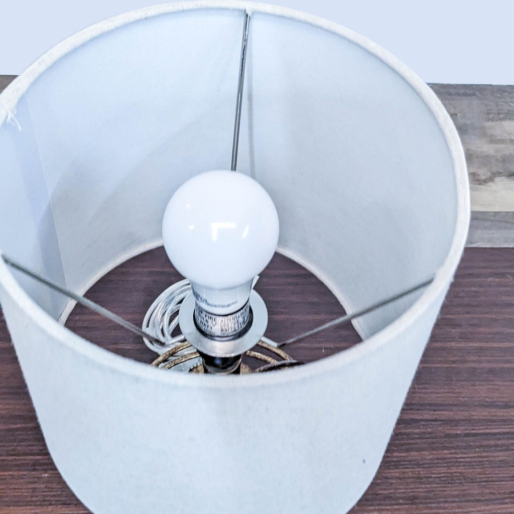 Close-up of Reperch lamp showing bulb and metal wire base under a white cylindrical shade.