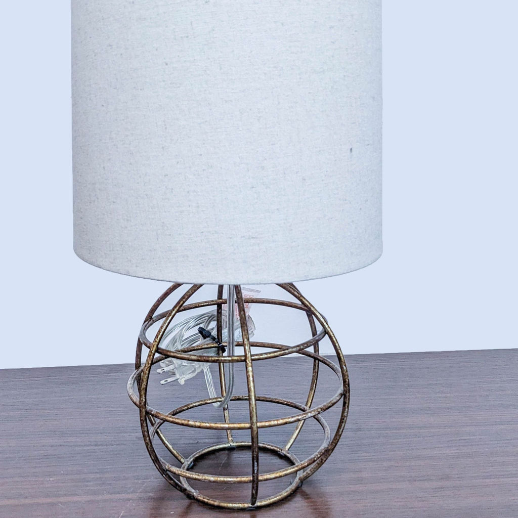 Table lamp with a white cylindrical shade and metal wire base on a wooden surface.