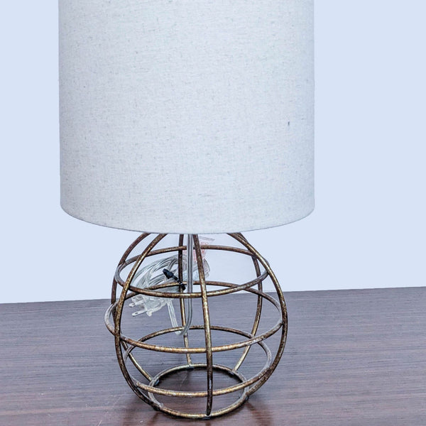 Table lamp with a white cylindrical shade and metal wire base on a wooden surface.
