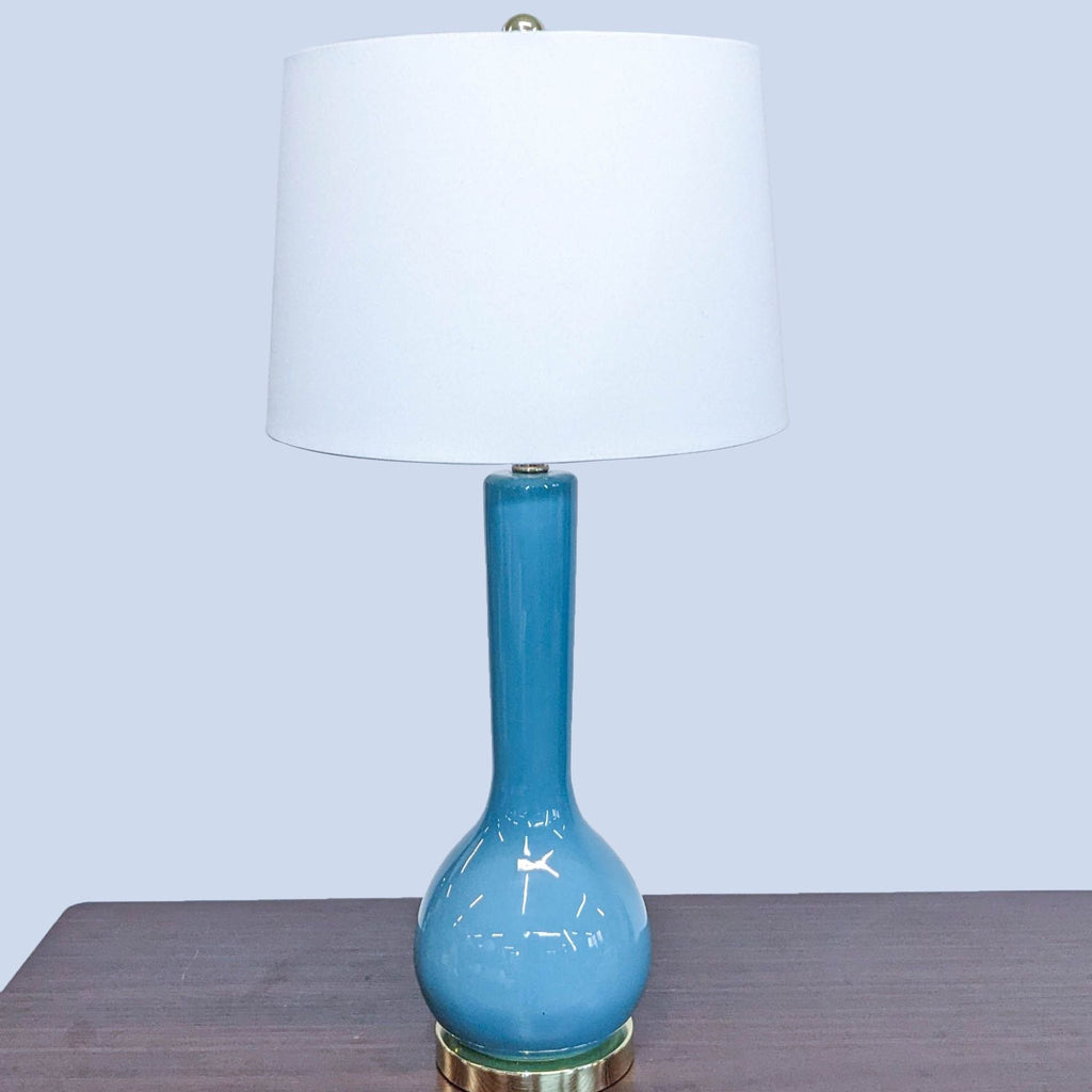 A blue ceramic lamp with a white shade on a table.