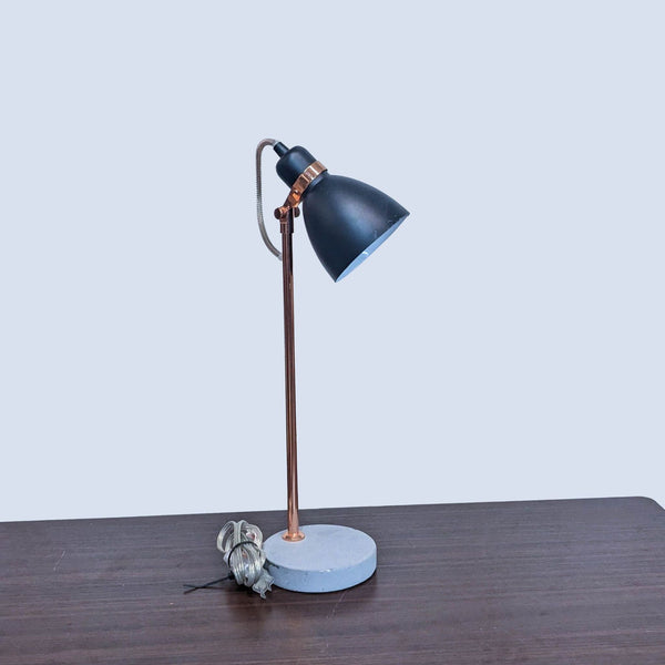 Reperch table lamp with black shade on wooden desk.