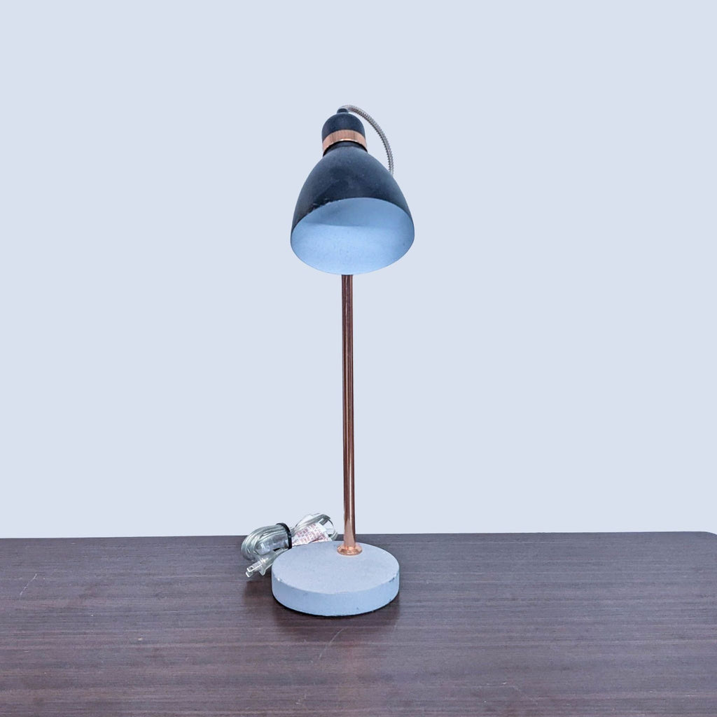 Front view of Reperch lamp on desk, black shade and round base.