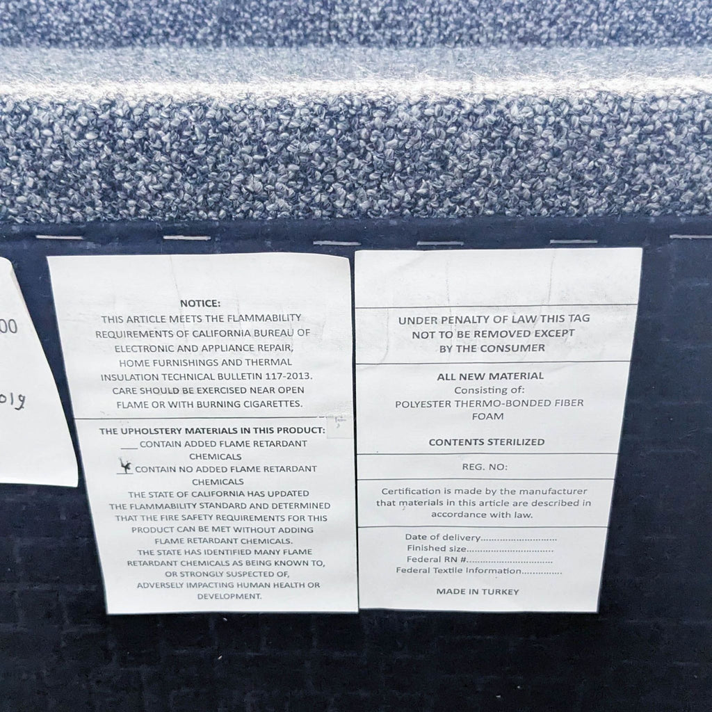 Close-up of the labels on a gray sofa's underside, detailing flammability and material info.