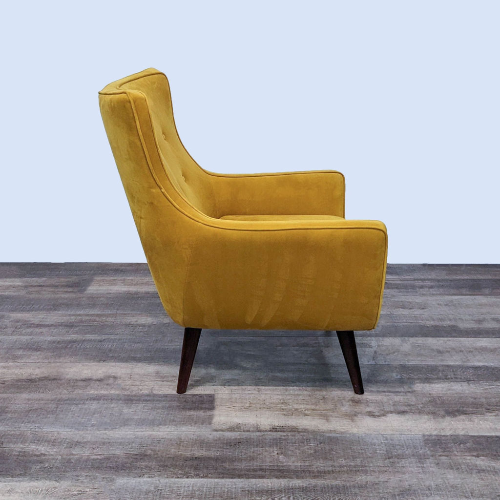 Side profile of a yellow velvet mid-century modern chair with dark tapered legs.