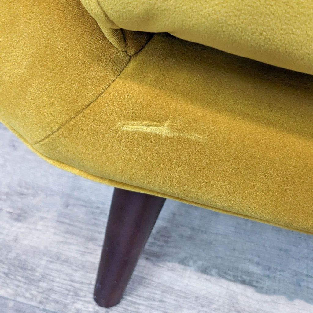 Close-up of yellow velvet chair detailing with dark wood tapered leg.