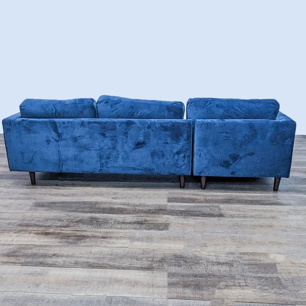 Back view of blue Reperch sectional sofa showing its tufted design and dark wooden feet against a light background.