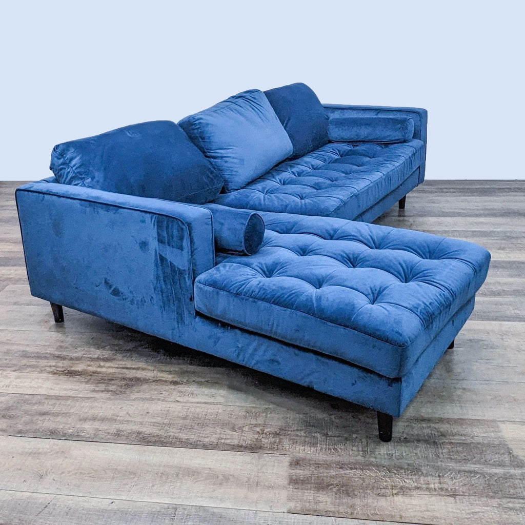 Side angle of blue Reperch two-piece tufted sectional with bolster pillows and dark finish legs on wood flooring.  