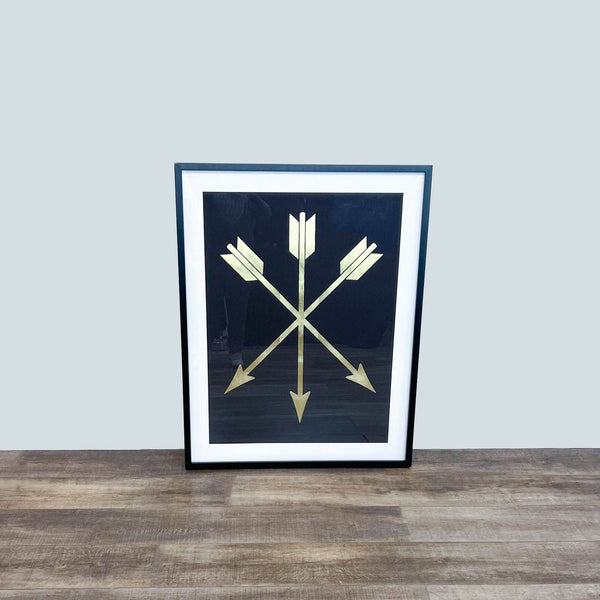 Framed print featuring gilded arrows on a black background, placed on a wooden floor.