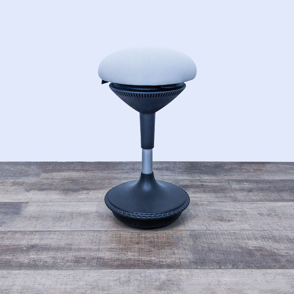 Adjustable office stool with dark base and padded seat on wooden floor.