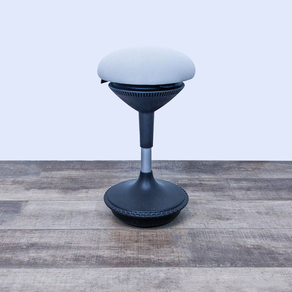 Adjustable office stool with dark base and padded seat on wooden floor.