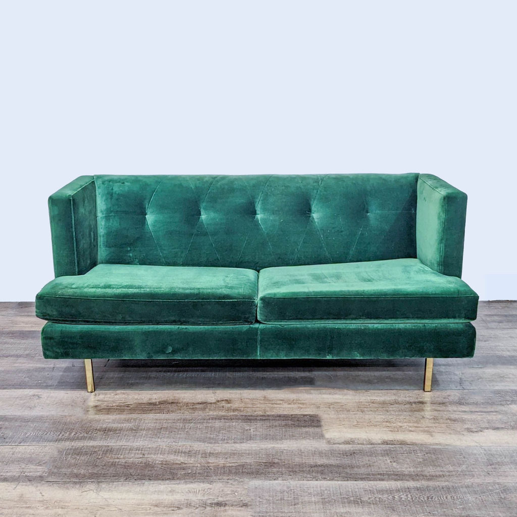 Emerald loveseat with tufted back and gold legs on wooden floor.
