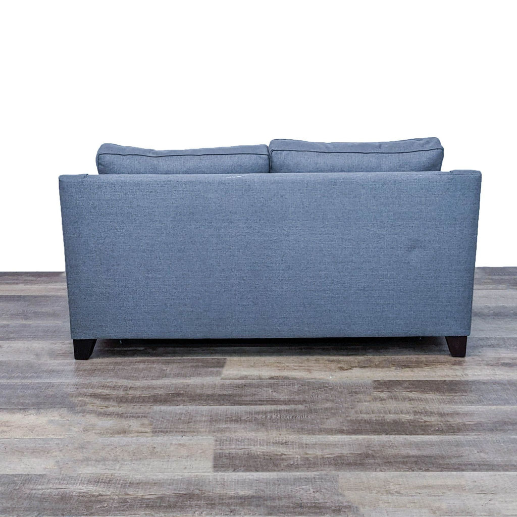 Back view of gray sleeper sofa with slope arms and cushion back on wooden floor.