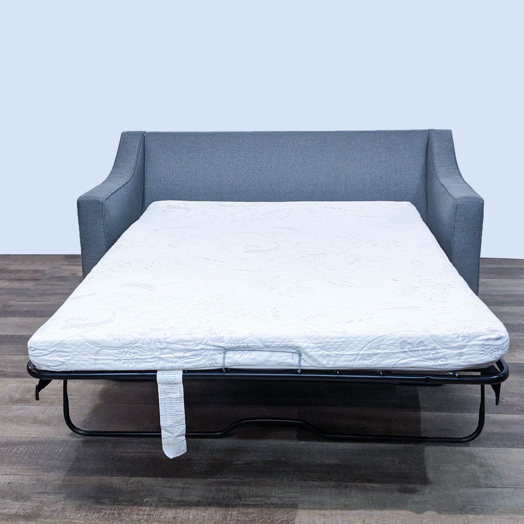 Sleeper sofa with a full mattress pulled out, featuring gray upholstery and dark finish feet.