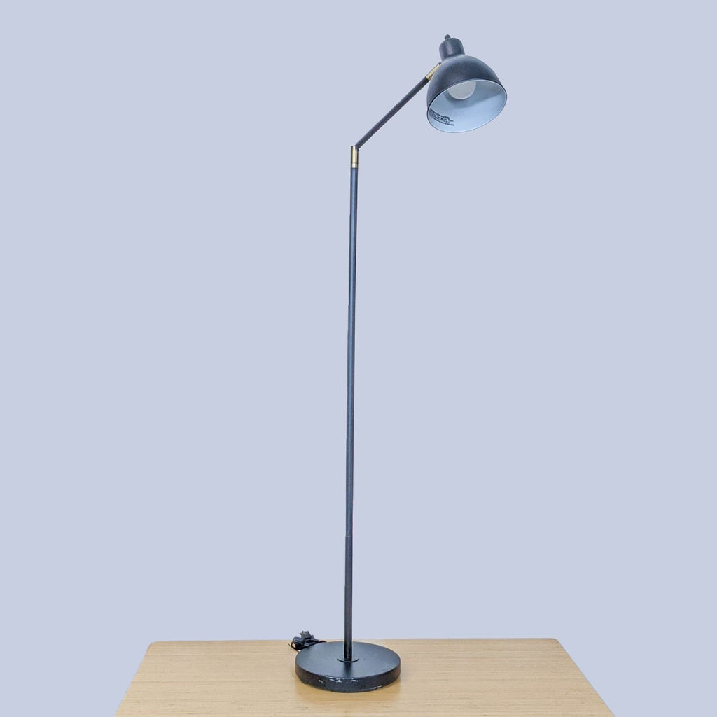 3. Sleek black Reperch floor lamp with a round base on a table.