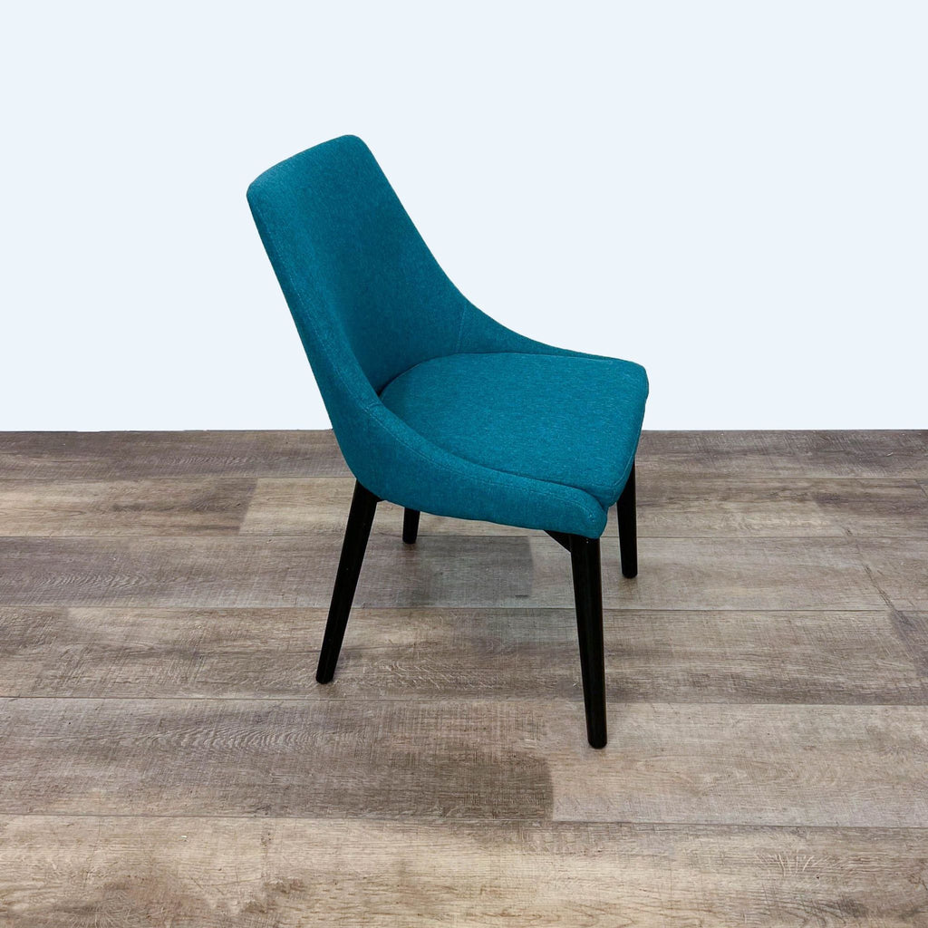 Side view of a teal upholstered dining chair on wooden legs.