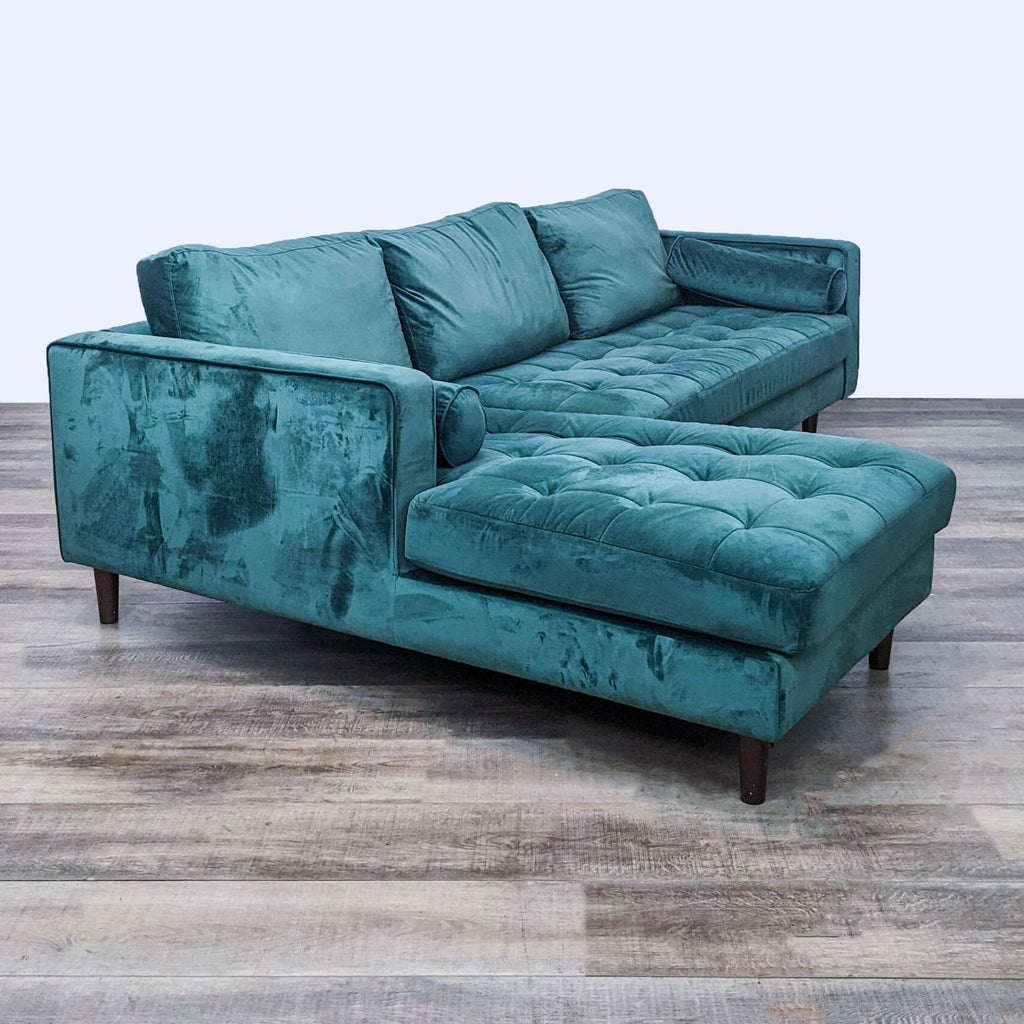 Side view of green velvet sectional, featuring a chaise and tapered legs.