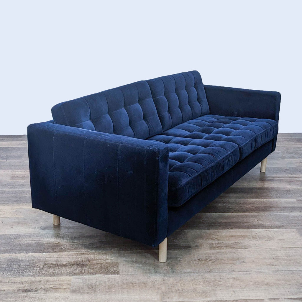 Side view of navy 3-seat tufted sofa with narrow arms, light wood feet.