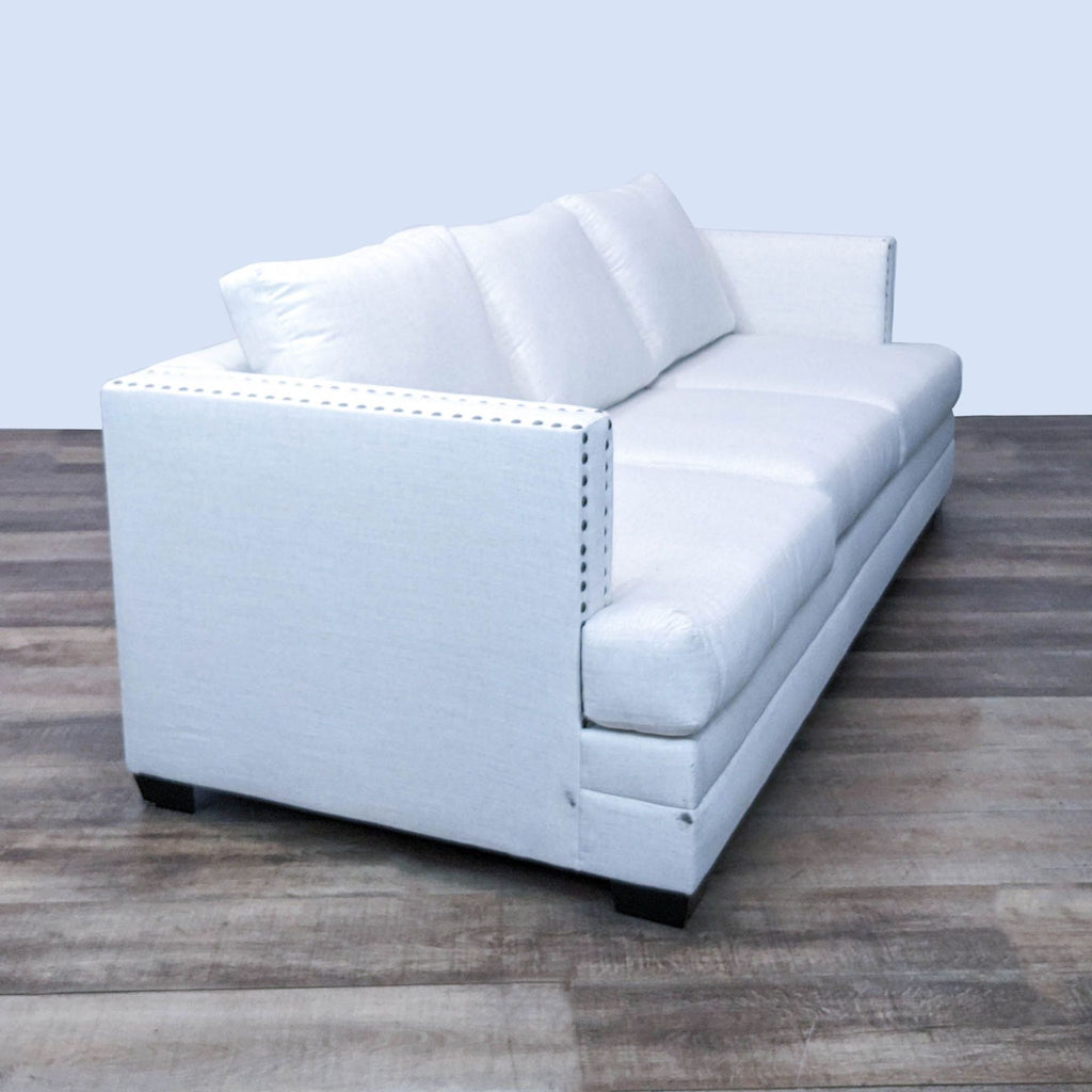 Side view of 3-seat sofa, featuring nailhead accents and dark wooden feet.