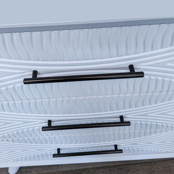 Close-up of white dresser drawers with black metal pulls. 