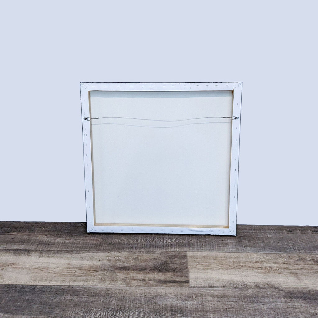 Back view of a square canvas with a hanging wire and white frame.