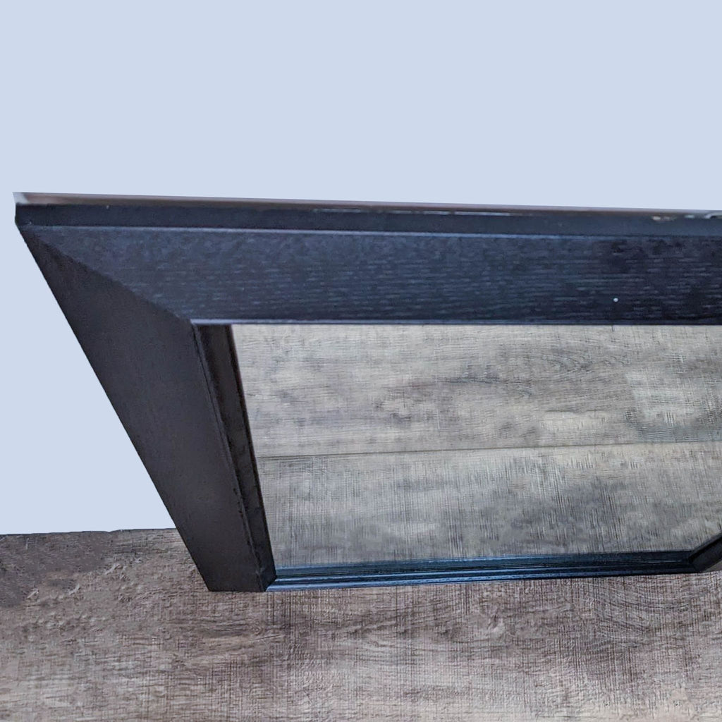 Close-up of a wood-framed mirror corner, showing its sleek design and dark-toned wood grain.