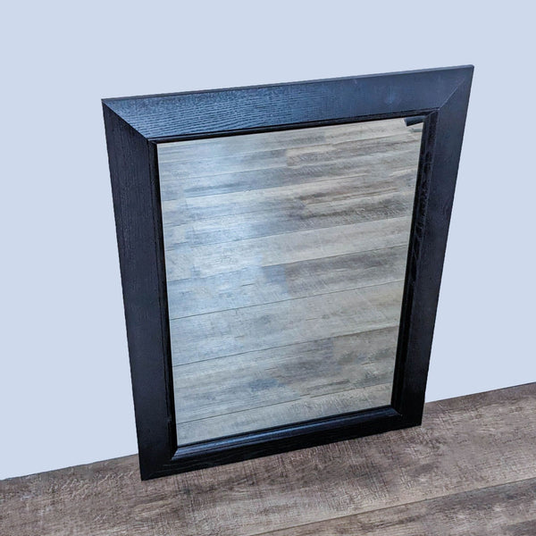 Wood-framed mirror with a polished surface and dark finish, leaning against a wooden floor.