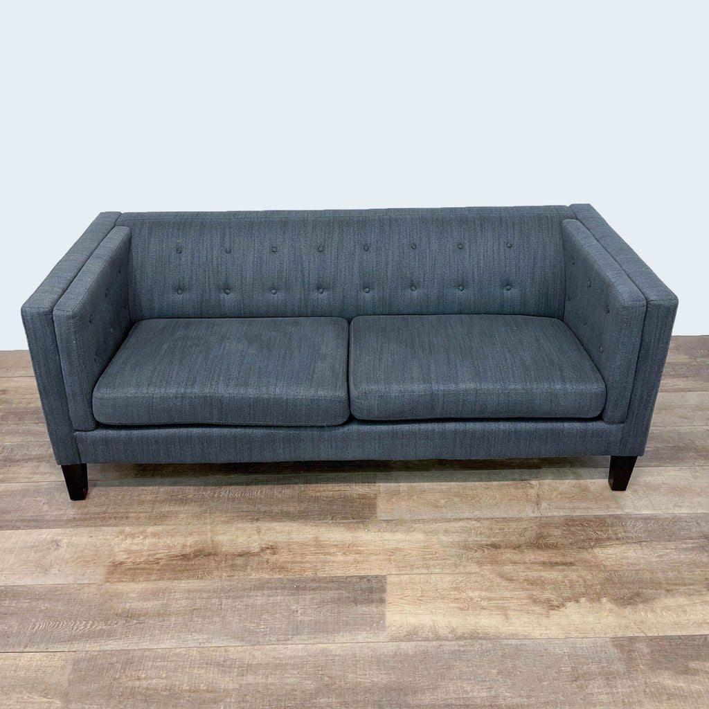 Gray tufted back sofa with dark legs on wooden floor.