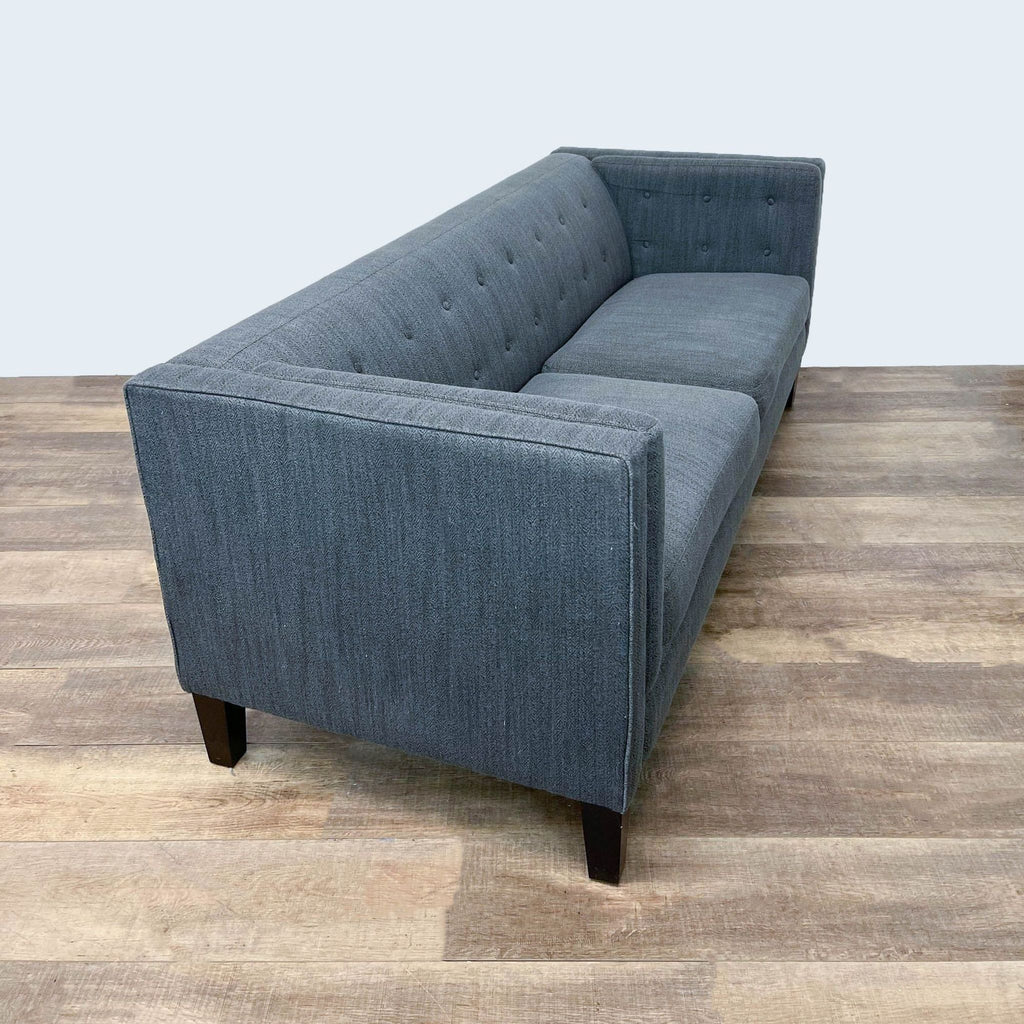 Side view of a gray 3-seater sofa with tufted back and dark wooden feet.