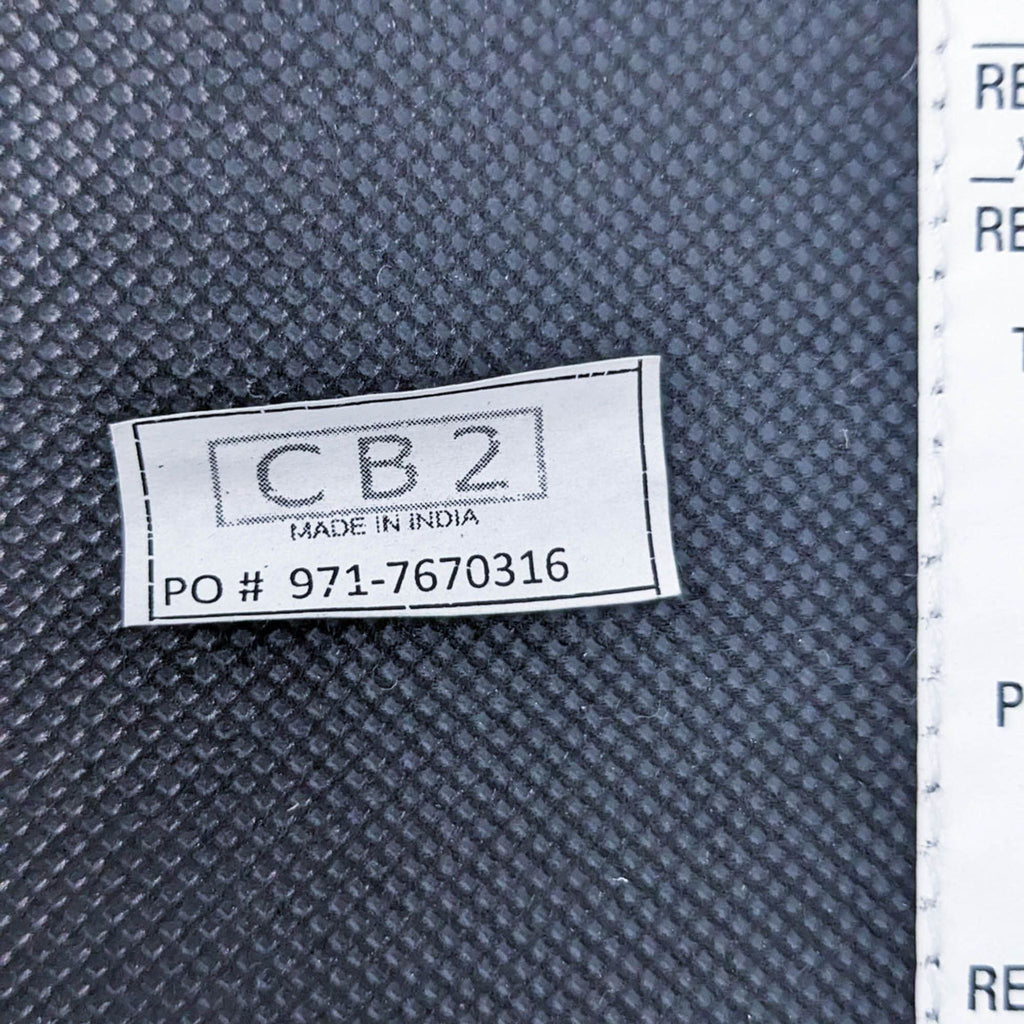 Label showing CB2 brand, Made in India, with PO number on dark textured fabric.