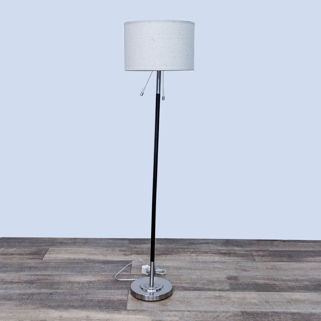 Slim floor lamp with a white drum shade on a wooden floor.