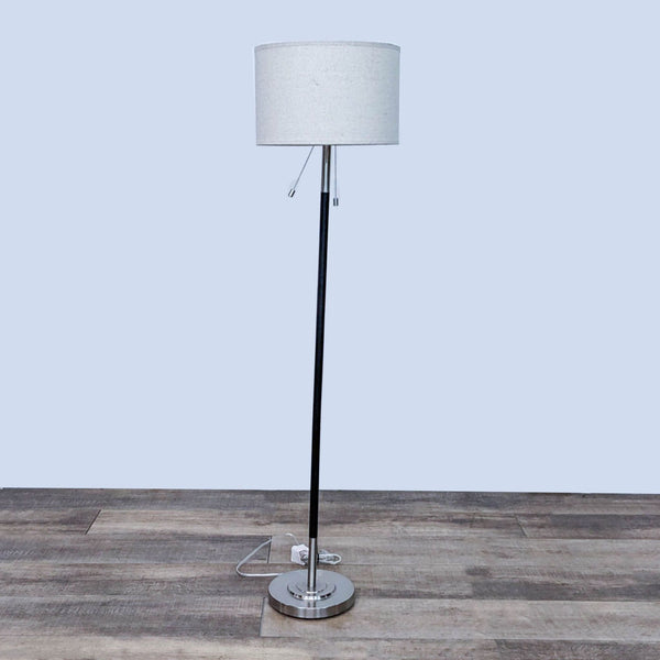 Slim floor lamp with a white drum shade on a wooden floor.