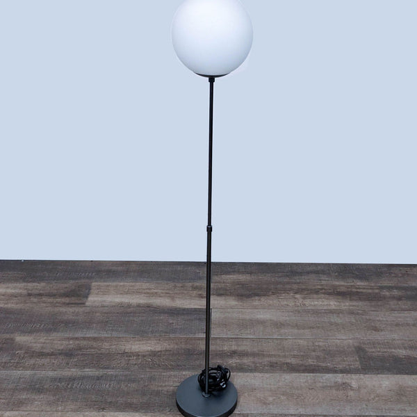 Tall black floor lamp with a round white globe light and circular base.