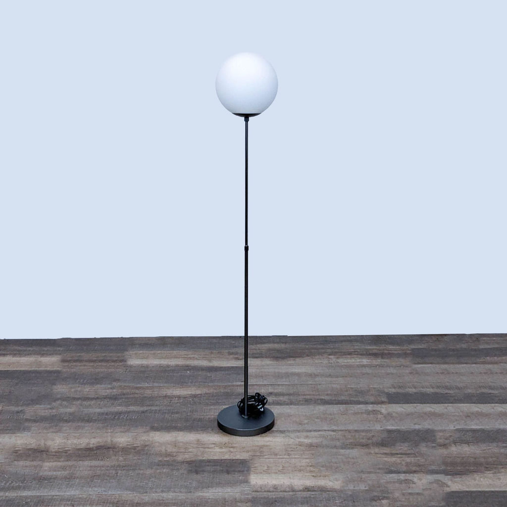 Minimalist floor lamp by Reperch with a spherical light on a slim black stand.