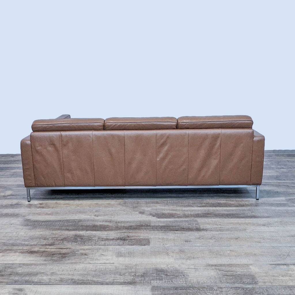 Back view of brown tufted leather sectional with chrome metal feet on wooden floor.