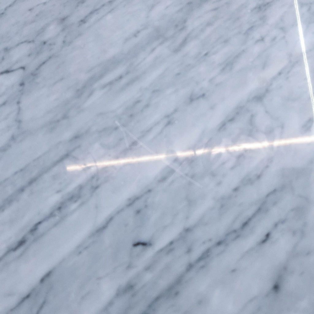 Close-up of marble tabletop showing light glare and a visible scratch.